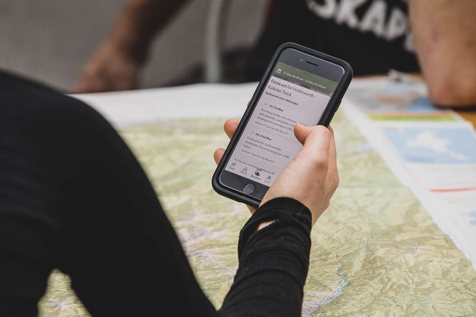 A tramper checking a track weather forecast on their phone over a paper map