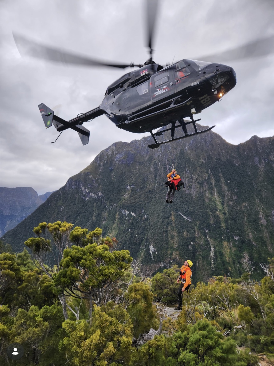 A rescue helicopter winching a person off a bush-clad ridge
